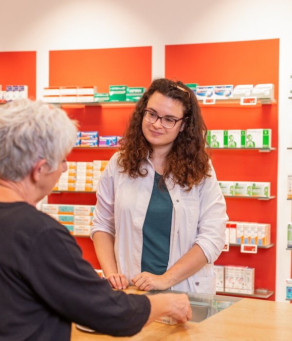 Kompetente Beratung an Ihrem Apothekentresen Eine Apothekerin im weißen Kittel berät eine Kundin an einem Tresen.