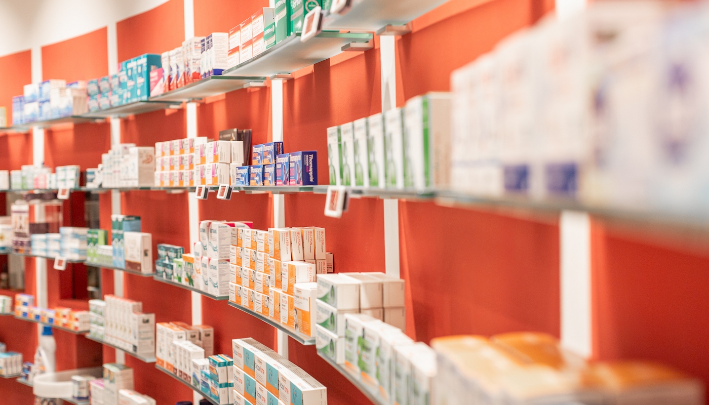 Produktregale in der Apotheke Nahaufnahme von Regalen in einer Apotheke, gefüllt mit Medikamenten in bunten Verpackungen. Die Regale sind vor einer roten Wand angeordnet und vermitteln einen gut organisierten Eindruck.